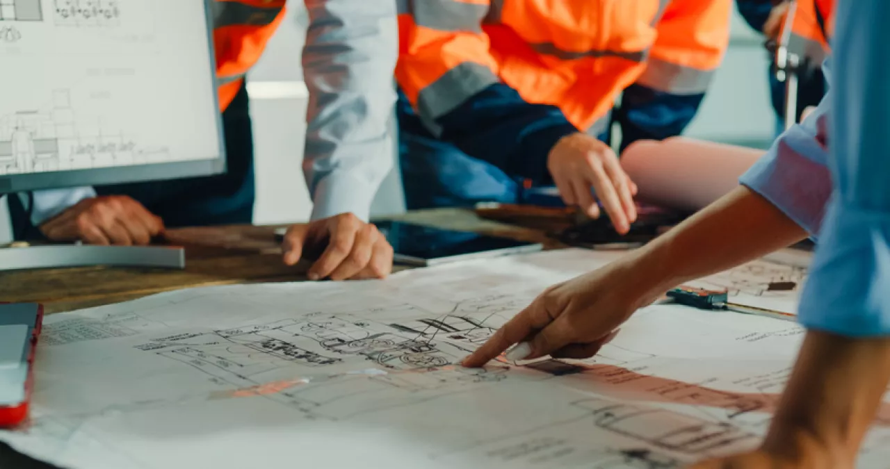 Closeup of team of engineers meeting to analyze blueprints.
